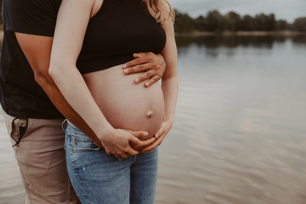 Babybauchfotos in berlin mit der Berliner Fotografin für Kinderfotografie Maria Brussig Lensofbeauty. fotos am See. Fotoshooting Babybauch im grünen. Wasser im Hintergrund. Paarfotos zusammen am See.