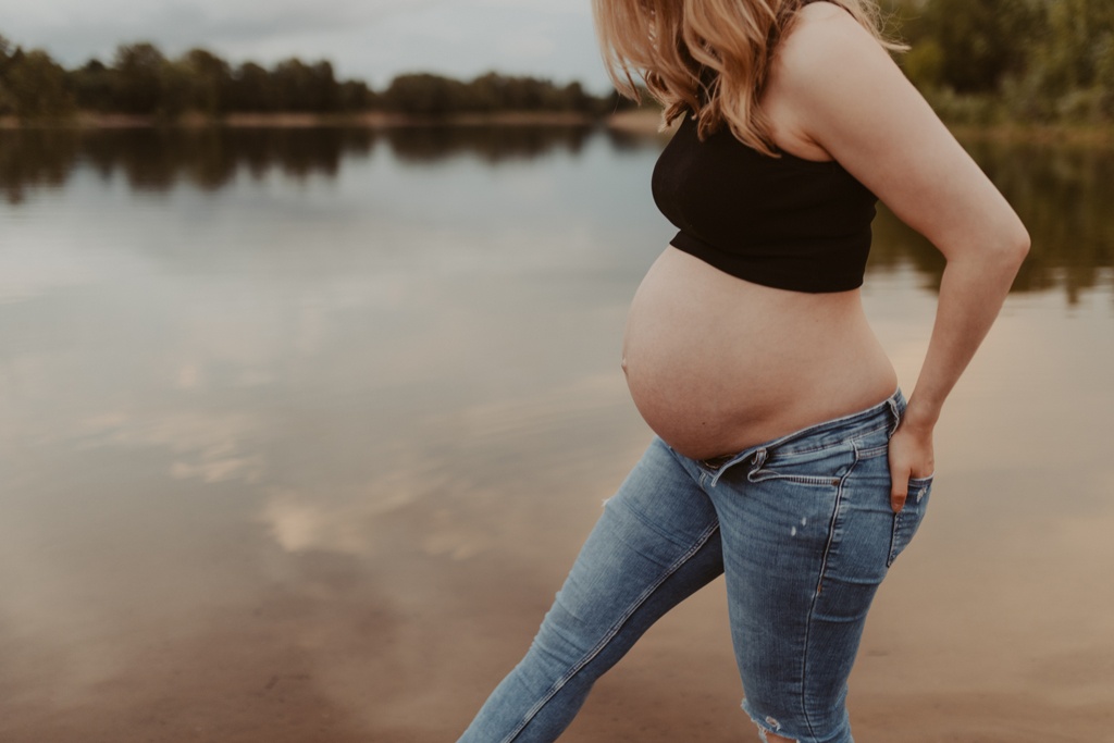 Babybauchfotos in berlin mit der Berliner Fotografin für Kinderfotografie Maria Brussig Lensofbeauty. fotos am See. Fotoshooting Babybauch im grünen. Wasser im Hintergrund. Paarfotos zusammen am See.