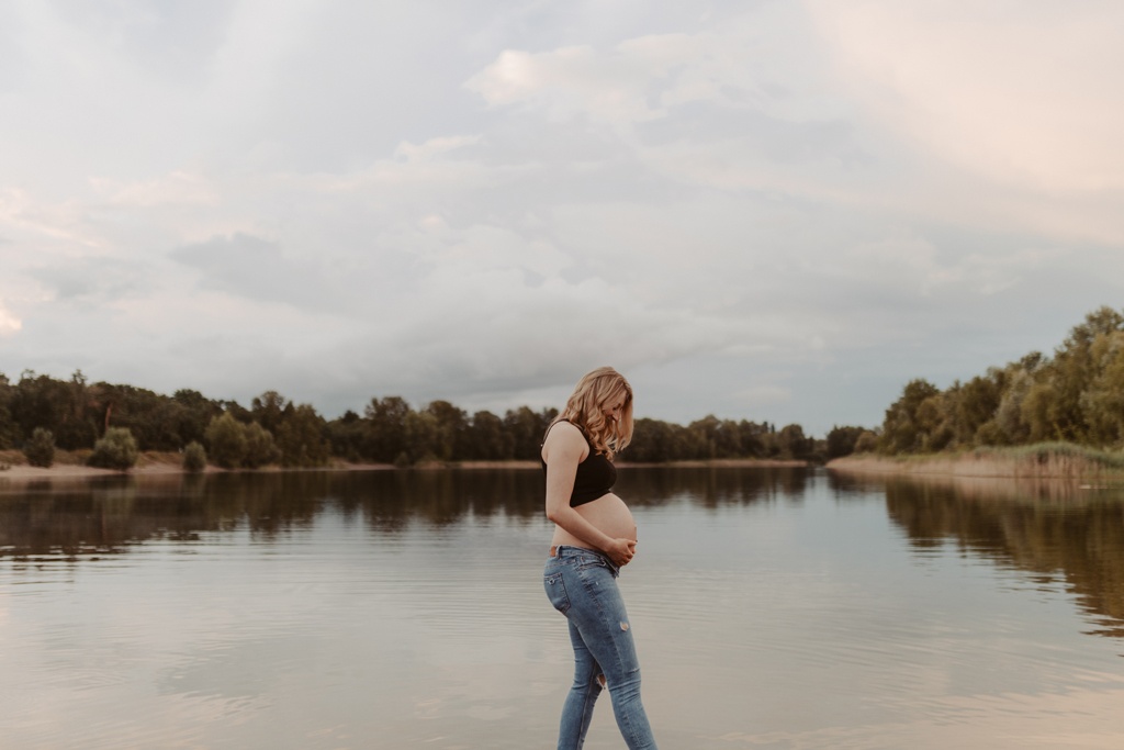 Babybauchfotos in berlin mit der Berliner Fotografin für Kinderfotografie Maria Brussig Lensofbeauty. fotos am See. Fotoshooting Babybauch im grünen. Wasser im Hintergrund. Paarfotos zusammen am See.