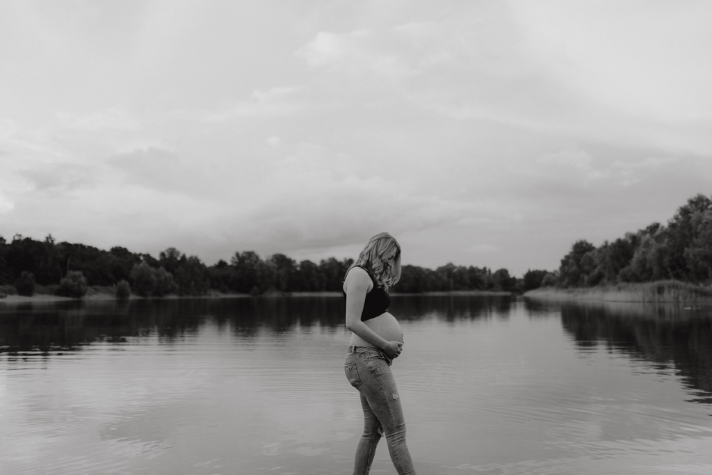 Babybauchfotos in berlin mit der Berliner Fotografin für Kinderfotografie Maria Brussig Lensofbeauty. fotos am See. Fotoshooting Babybauch im grünen. Wasser im Hintergrund. Paarfotos zusammen am See.