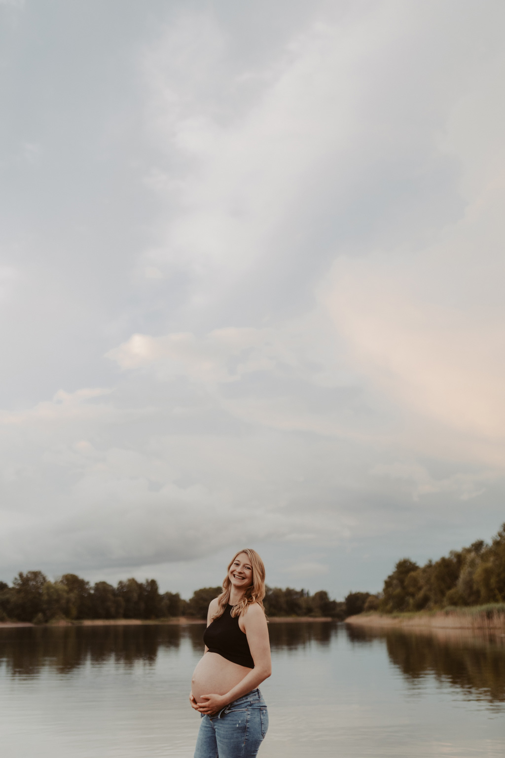 Babybauchfotos in berlin mit der Berliner Fotografin für Kinderfotografie Maria Brussig Lensofbeauty. fotos am See. Fotoshooting Babybauch im grünen. Wasser im Hintergrund. Paarfotos zusammen am See.