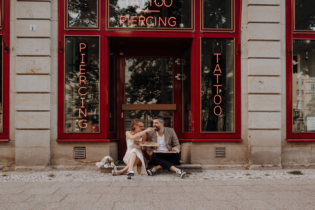 Hochzeit in berlin an der Frankfurter Allee mit Fernsehturm im Hintergrund und Tattoo und Piercing studio. Eheringe auf pizza. Paarfotos in berlin. Hochzeit mitten in berlin. außergewöhnliche Festival rock Hochzeit. Festival Hochzeit. rock Hochzeit.